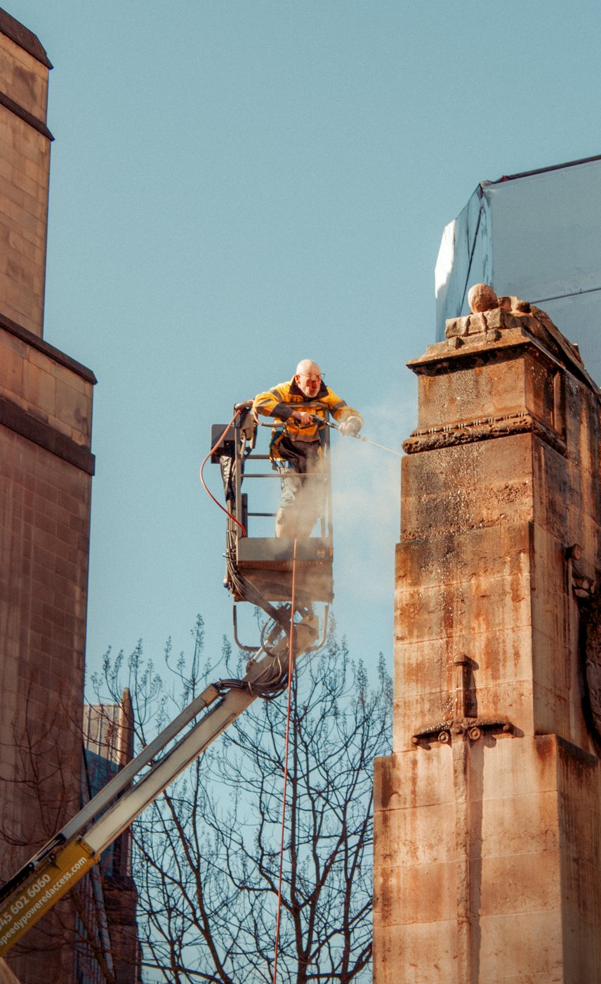 Construction worker on a cherry picker cleaning stonework in Manchester
